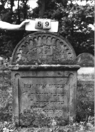 Grabstein 59 (Index: 100110844) Material: Sandstein Zustand: im Giebel stark verwittert mit großem Textverlust, sonst kleine Abschieferungen, am unteren Rand abgebrochen Maße HxBxT: 116x80x16 cm Beschreibung: Stele, Rundbogenabschluß mit Rundbogenfries und Verdachung, Schriftfelder eingetieft: Grabstein 59