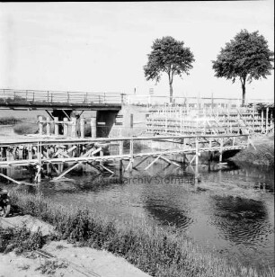 Trave: Brückenneubau: rechts Holzgerüstbau für neue Brücke: vorn Notsteg: im Hintergrund alte Holzbrücke und zwei Bäume