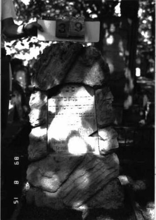 Grabstein 39 (Index: 100105482) Material: Muschelkalk, weiße Marmorplatte Zustand: Platte mehrfach gesprungen und Teile herausgebrochen Maße HxBxT: 106x43x26 cm Beschreibung: Stele, rustica, konische Schriftplatte mit Segmentbogenabschluß: Grabstein 39