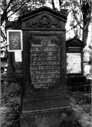 Grabstein 305 (Index: 100112006) Material: Sandstein Zustand: leicht verwittert Maße HxBxT: 151x60x27 cm Beschreibung: Stele, getreppter Sockel, giebelartiger Abschluß mit Verdachung, rechteckiges Schriftfeld eingetieft mit rund eingezogenen Ecken Symbolik: Kranz mit Schleife: Grabstein 305