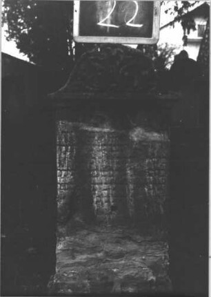 Grabstein 22 (Index: 100112309) Material: Sandstein Zustand: stark beschädigt und verwittert, zerbrochen und repariert Maße HxBxT: 93x35x8 cm Beschreibung: Stele, Sockel, Konvexbogenabschluß Symbolik: florale Ornamente im Abschluß: Grabstein 22