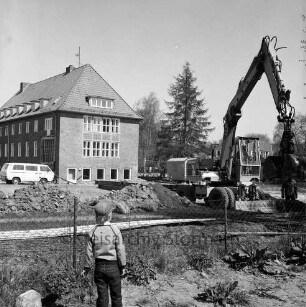 Woldenhorn-Schule: Sonderschule des Kreises Stormarn für geistig behinderte Kinder: Ecke Reeshoop / Schulstraße: Erweiterungsbau: in Bau: Bagger bei Ausheben der Baugrube: Arbeiter, Aushub, Eisenträger, Bretter, Bauwagen, Kleintransporter: hinten Altbau: Blick von Hans-Schadendorff-Stieg aus: im Vordergrund Kind bei Blick durch Maschendrahtzaun