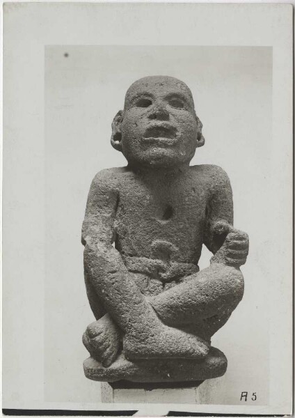 Stone figure (made of Tezontli lava stone) with folded legs, wide open mouth, pubic bandage, ear jewellery, round hole on the chest (for an ornamental stone?), perhaps representing the god Xipe. Height: 42 cm