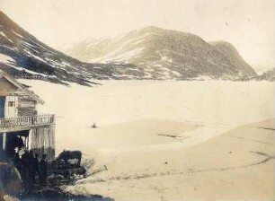 Norwegen. Blick auf den zugefrorenen Djupvassee mit Einheimischen an Schlitten vor einem Holzhaus
