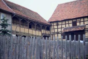 Blick über Zaun in einen Hof; Laubenganghaus und Scheune