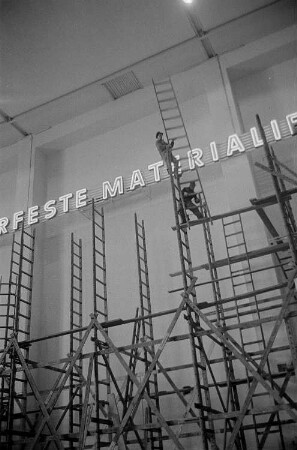 Aufbauarbeiten zur Leipziger Frühjahrsmesse, Arbeiter montieren eines Gerüstes, im Hintergrund der Schriftzug "Feste Materialien"