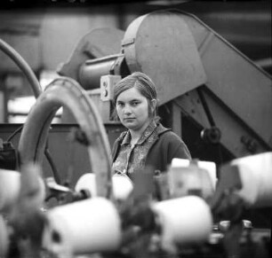 Junge Fabrikarbeiterin : VEB Wurzener Teppichfabrik. Portrait einer jungen Fabrikarbeiterin, zwischen den von ihr zu bedienenden Maschinen