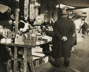 Auf einem Weihnachtsmarkt. Ein Mann betrachtet die Auslagen eines Standes. Es werden diverse Weihnachtsartikel angeboten