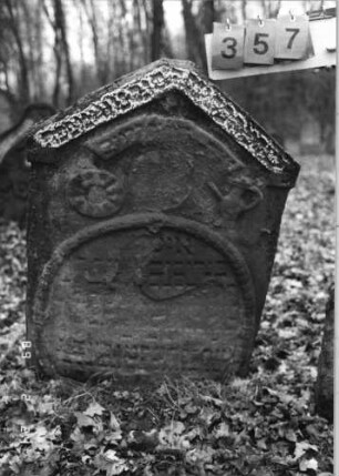 Grabstein 357 (Index: 99752570) Material: Sandstein Zustand: abgeblätt. /stark verwitt/großer Textverl Maße HxBxT: 100x72x10 cm Beschreibung: Stele, giebelartiger Abschluß, ovales Schriftfeld Symbolik: Levitenkanne mit Schale, Lorberkranz um Schriftfeld, Schriftband: Grabstein 357