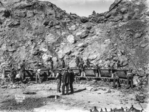 Szenerie im Bergwerk : Blick auf die Szenerie in einem Bergwerk. Förderwagen stehen zum Abstransport des Gesteins bereit. Im Vordergrund berät sich eine Gruppe von leitenden Personen.