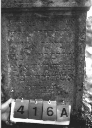 Grabstein 416 (Index: 99800294) Material: Sandstein Zustand: stark verwittert Maße HxBxT: 108x56x12 cm Beschreibung: Stele, Abdeckplatte, Rundbogenaufsatz, in Voluten auslaufend, Schriftfeld eingetieft, Sockel Symbolik: zwei Blumen, Blüten: Grabstein 416A