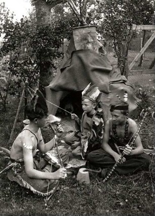 Drei Jungen beim Indianerspiel in einem Garten (bem Pfeiferauchen vor dem Tipi- "Hier gibt es guten Tabak")