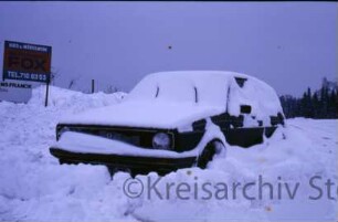 im Winter: eingeschneites Auto, Firmenschild Kies- und Mörtelwerk, hoher Schnee