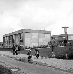 Realschule [später: Friedrich-Junge-Schule]: Sieker Landstraße: vorn Mitte und links auf Weg mehrere Schulkinder: rechts Straßenlampe: dahinter Grünanlage: dahinter Reihe von Fahrrädern: hinten Schulgebäude
