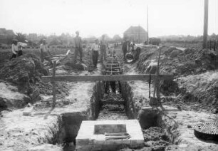 Güstrow. Bau eines Abwasserkanals. Blick auf den teilweise gefüllten Graben mit Grabensicherung und gemauertem Kontrollschacht