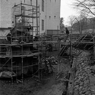 Restaurierung: Sanierung Mauerwerk an Turmfuß: Arbeiter auf Gerüst, Schubkarren: innerer Graben: neue Grabenversteifung mit Holzbohlen am Grabenfuß: Grabenböschung nach Wiederherstellung mit alten Findlingen: im Hintergrund Lübecker Straße, Bauernbrücke, Kastanienallee