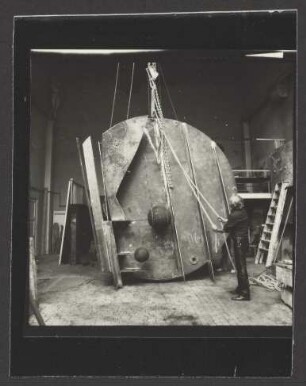 Fotografie von Bernhard Heiliger mit der Skulptur „Auge der Nemesis“ an einer Seilwinde in seinem Hochschulatelier