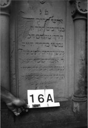 Grabstein 16 (Index: 99804463) Material: Sandstein Zustand: stark verwittert und abgeblättert Maße HxBxT: 176x63x32 cm Beschreibung: ädikulaartige Stele mit Halbsäulen, getreppter Sockel, Abschluß mit Zinnenaufsatz, Schriftfeld mit Maßwerk Symbolik: stilisierte Blätter, Maßwerk Besonderheit: kulturhistorisch wertvoll / künstl.-formale Gründe (Ornamentik, Form): Grabstein 16A