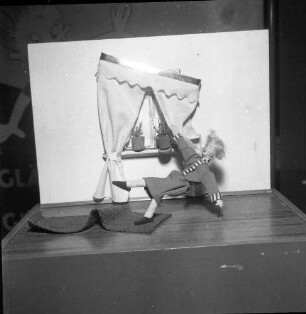 Ausstellung zum Thema Vermeidung häuslicher Unfälle. Vitrine mit Darstellung eines Sturzes über einen Teppich
