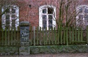 Dorfstraße 32: Bauernhaus aus Backstein: Wohntrakt mit Segmentbogen-Sprossenfenstern, Teilansicht: vorne Grundstücksmauer mit Holzzaun