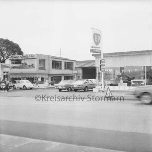 Autohaus Bruno König & Co.: Hamburger Straße: BP-Tankstelle und Opel-Reparatur-Werkstatt: links Zapfsäulen und VW Käfer: dahinter Geschäft und Verwaltungsbau mit Firmennamen: rechts Gebäude mit Verkaufsraum: davor und darin Opel-Pkws: in der Mitte Tankstellenschild