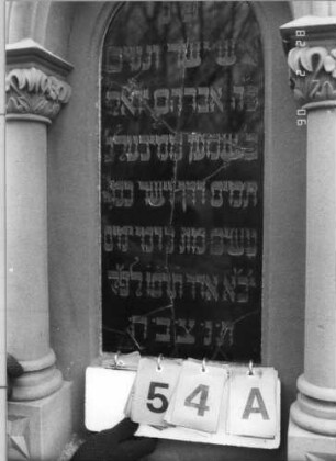 Grabstein 54 (Index: 100114898) Material: Sandstein und polierter Granit Zustand: Stele verrutscht, Texttafel mehrfach zerbrochen und repariert Maße HxBxT: 263x71x36 cm Beschreibung: Ädikula mit gestuftem Sockel auf Rustikasockel, eingezogener Spitzgiebel mit Akroteren und Laubdekor, eingesetzte Texttafel: Grabstein 54A