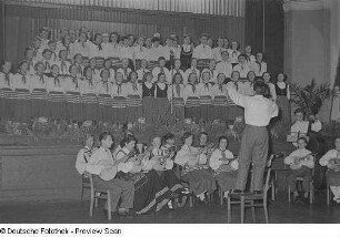 Orchester, Chor sowie ein Chorleiter auf einem Stuhl des Pionierensembles "Julian Marchlewski" der Humboldtschule bei einer Kulturveranstaltung