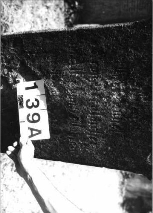 Grabstein 139 (Index: 100085471) Zustand: stark verwittert mit Textverlust Maße HxBxT: 130x50x27 cm Beschreibung: Stele, Sockel, giebelartiger Abschluß mit Verdach.: Grabstein 139A