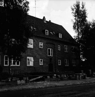Hebbelstraße: Ausbau: vorn unbefestigte Straße, Stapel mit Gehwegplatten und Mülleimer: dahinter Wohnhäuser der Gemeinnützigen Baugenossenschaft Bad Oldesloe mit Vorgärten