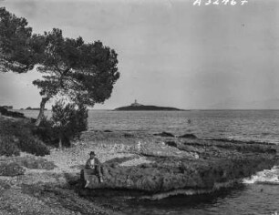 Am Meer : Mann auf Felsen am Meer sitzend. Im Hintergrund eine Insel mit Leuchtturm