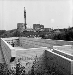 Zentralklärwerk: Anna-Heitmann-Weg: vorne Vorklärbecken nach Fertigstellung: im Hintergrund Faulturm in Bau, Rohbau mit Gerüst, Baukran, Stapel mit Baumaterialien: oben Vorklärbecken mit Laufsteg, Betriebsgebäude: hinten rechts Holzbaracken, Stromleitungen: im Hintergrund Wohnhaus
