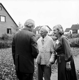 Hermann Claudius: Schriftsteller: geboren 19. Oktober 1878, gestorben 8. September 1980: 99. Geburtstag: Vorgarten von Wohnhaus: Jubilar mit Ehefrau Gisela Claudius bei Begrüßung des Gratulanten Ministerpräsident Gerhard Stoltenberg: hinten Blumenrabatte, Wohnhäuser, 24. Oktober 1977