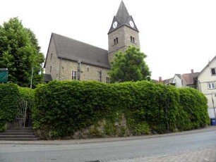 Treis an der Lumda-Evangelische Kirche - Ansicht von Südwesten mit Kirche (Spätromanische Gründung 13 Jh) über Kirchhofmauer (stark überwachsen-Wehrgang mit Steinbrüstung und Schießscharten abgetragen)