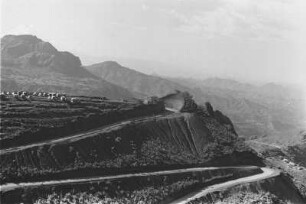 Abfall des Simien Gebirges : Bergstraße im Simien Gebirge in Richtung Debark. Rechts im Bildhintergrund ein Zeltlager, möglicherweise ein Straßenarbeitercamp.