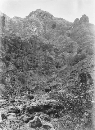 Landschaft : Blick auf eine felsige Landschaft. Mittig auf einem Felsen sitzend ein winkender Mann