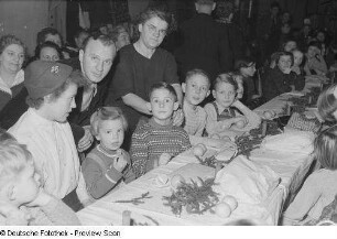 Eltern und beschenkte Kinder an einer geschmückten Tafel bei der Weihnachtsfeier des Verlags Volk und Wissen