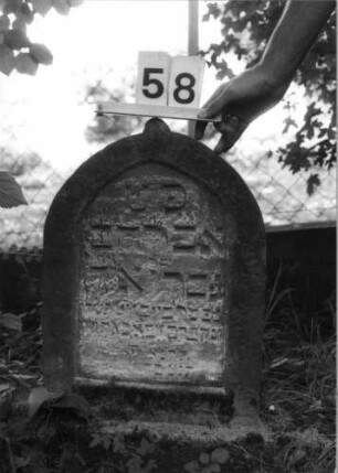 Grabstein 58 (Index: 100100598) Material: Sandstein Zustand: verwittert Maße HxBxT: 68x42x8 cm Beschreibung: Stele, Spitzbogenabschluß mit kleinem Mittelakroter Besonderheit: Kindergrab: Grabstein 58