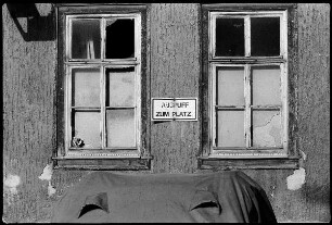 Verhülltes Auto und Hausfassade mit Schild "Auspuff zum Platz"