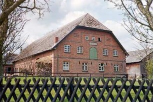 Bundesstraße (20): giebelständiges Bauernhaus aus Backstein: Straßenfront mit Sprossenfenstern, in Obergeschoss Ladeluke: Traufseite, an Hauswand Holzstapel, hinten links Querbau mit Tor: rechts Nebengebäude mit Verbretterung: vorne Jägerzaun
