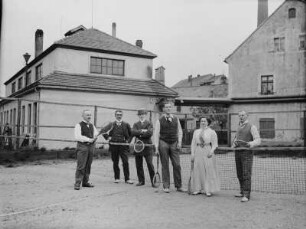 Portrait einer Gruppe mit Männern und einer Frau auf einem Tennisspielfeld