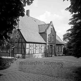Pastorat: Matthias-Claudius-Straße: Matthias-Claudius-Geburtsstätte [Nachfolgebau von Geburtshaus des Dichters Matthias Claudius]: vor Giebelwand Gartenbank: Plattenweg: Bäume