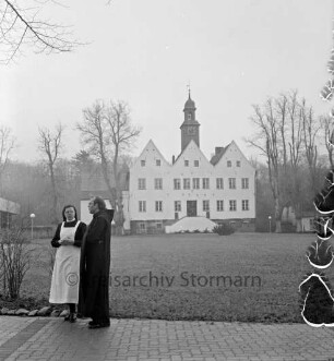 Kloster Nütschau: Herrenhaus: Nordfront mit Außentreppe: davor Rasenfläche: rechts und links Bäume: vorn links Pater Subprior Matthäus Buß und Clemens-Schwester im Gespräch