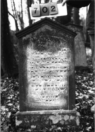 Grabstein 702 (Index: 99752358) Material: Sandstein Zustand: leicht verwitt/abgeblätt. m. Textverlust Maße HxBxT: 114x52x7 cm Beschreibung: Sockel, giebelart. Abschluß mit Verdach. , Schrift eingetieft m. Segmentbogenabschluß: Grabstein 702