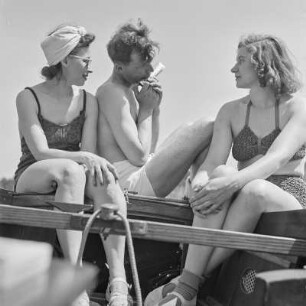 Elisabeth Gremmler (links) und ein befreundetes Paar sitzen auf einem Segelboot, der Mann spielt Mundharmonika