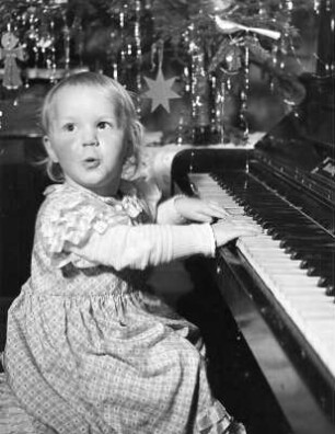 Kinderbilder. Kleines Mädchen am Klavier vor dem Weihnachtsbaum