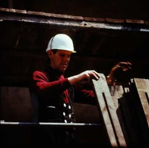 Zimmerer auf einem Gerüst beim vertikalen Weiterreichen eines Holzbrettes