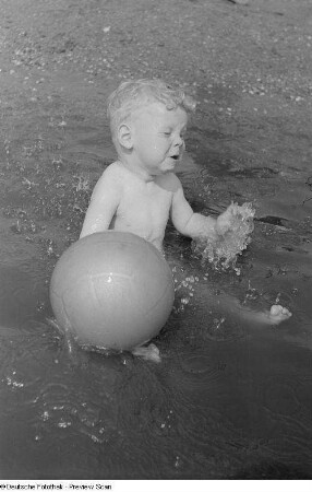 Kleiner Jungen, mit einem Ball im Wasser spielend