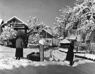 Winterbilder. Verschneite Dorfstraße. Frauen an einem Brunnen