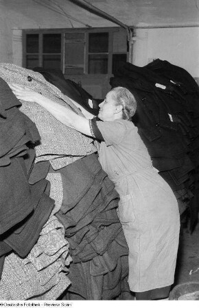 Portrait einer Frau beim Stapeln von Trenchcoats im VEB Bekleidungswerk Leipzig