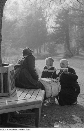 Eine Frau und ein Mädchen sowie eine Frau auf einer Parkbank mit Kinderwagen